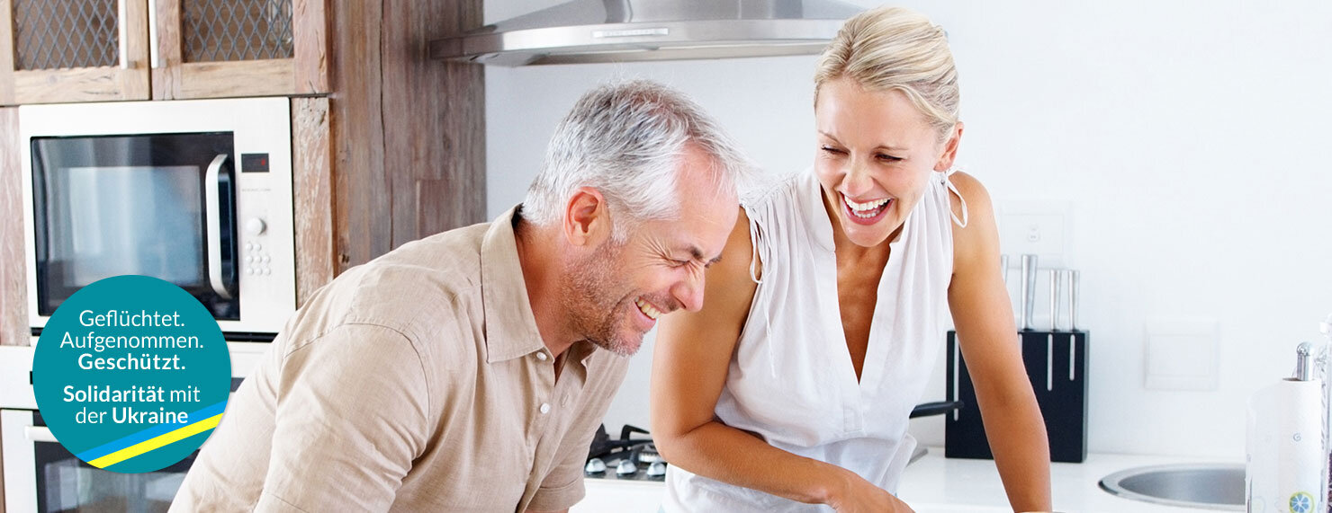 IDEAL Hausratversicherung: Frau und Mann lachen in der Küche beim Kochen