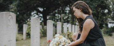 Frau mit Blumenstraß kniet vor Grab