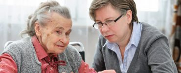 Eine alte Dame puzzelt mit einer Pflegerin des Pflegeheims am Tisch