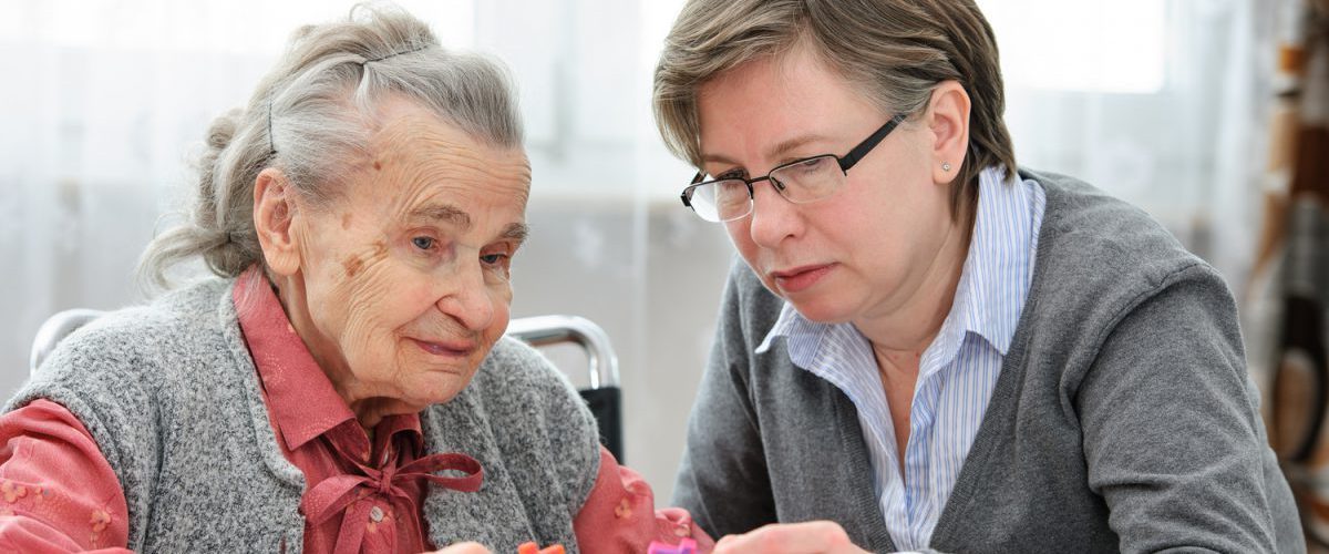 Eine alte Dame puzzelt mit einer Pflegerin des Pflegeheims am Tisch