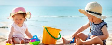 Zwei Kleinkinder spielen am Strand in der Sonne mit ausreichend Sonnenschutz