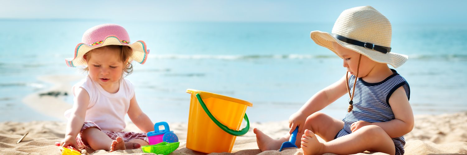 Zwei Kleinkinder spielen am Strand in der Sonne mit ausreichend Sonnenschutz