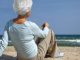 Frau am Strand sitzend und aufs Meer blickend