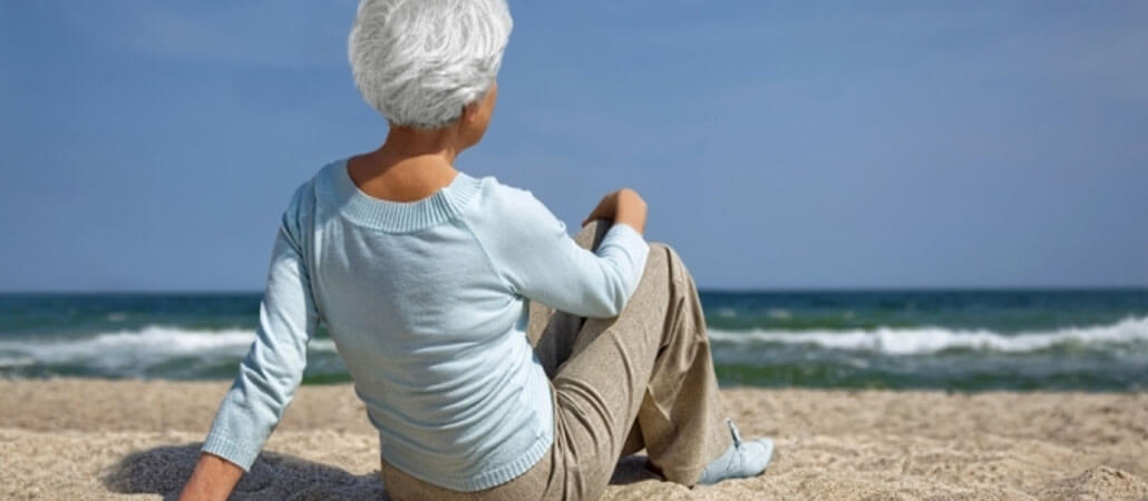 Frau am Strand sitzend und aufs Meer blickend