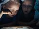 Kinder schauen heimlich in der Nacht unter einer Decke ins Internet