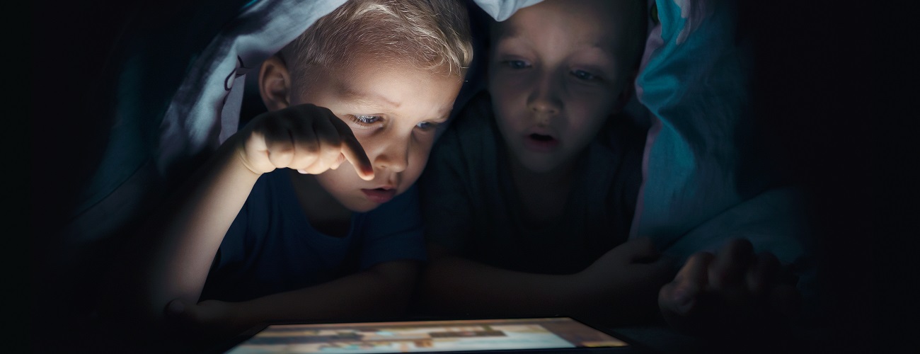 Kinder schauen heimlich in der Nacht unter einer Decke ins Internet