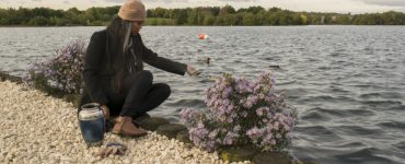 Ein Mensch sitzt am Ufer und streut Asche ins Wasser