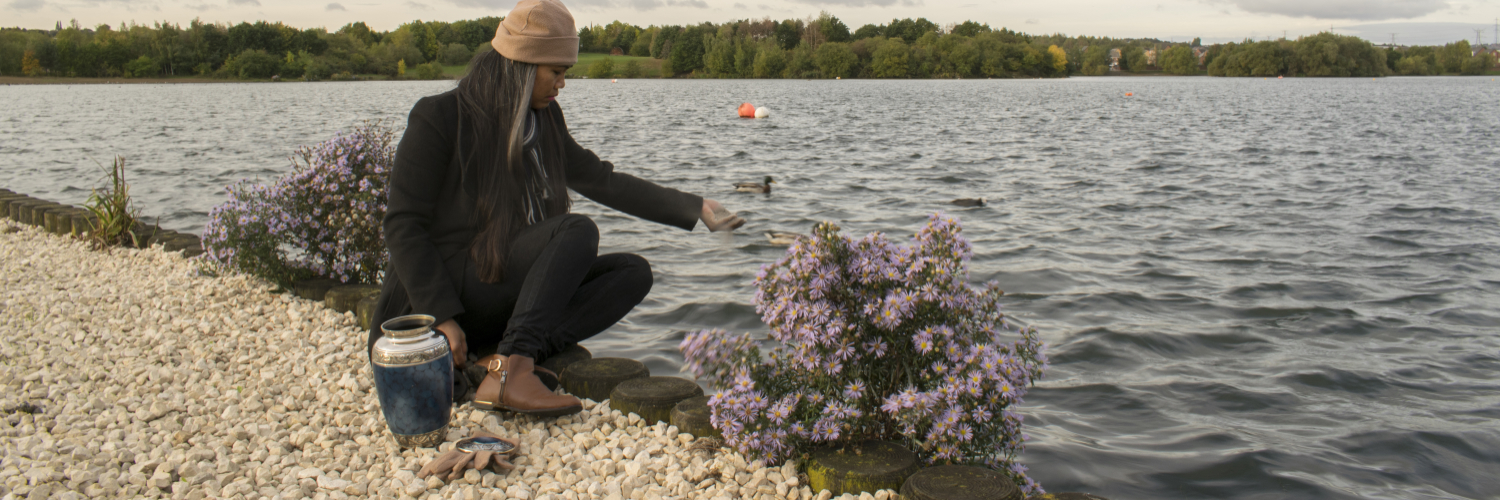 Ein Mensch sitzt am Ufer und streut Asche ins Wasser