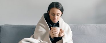 Frau mit Tee und Decke auf Sofa