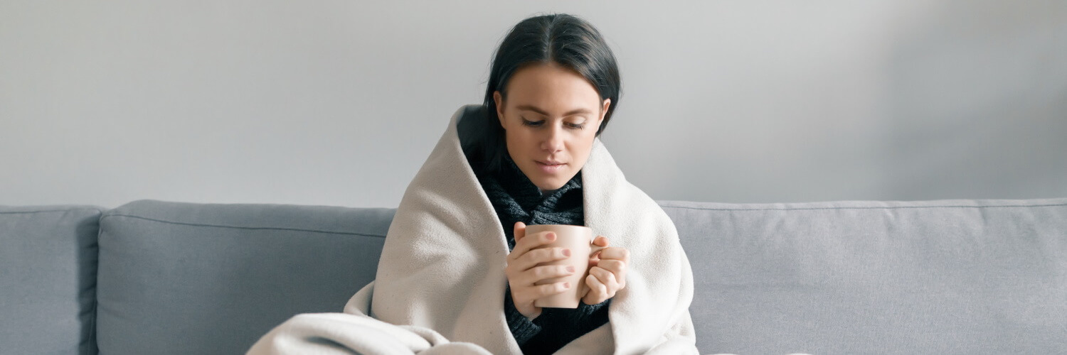 Frau mit Tee und Decke auf Sofa