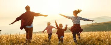 Eine vierköpfige Familie läuft auf einem Feld in Richtung der untergehenden Sonne