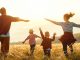 Eine vierköpfige Familie läuft auf einem Feld in Richtung der untergehenden Sonne