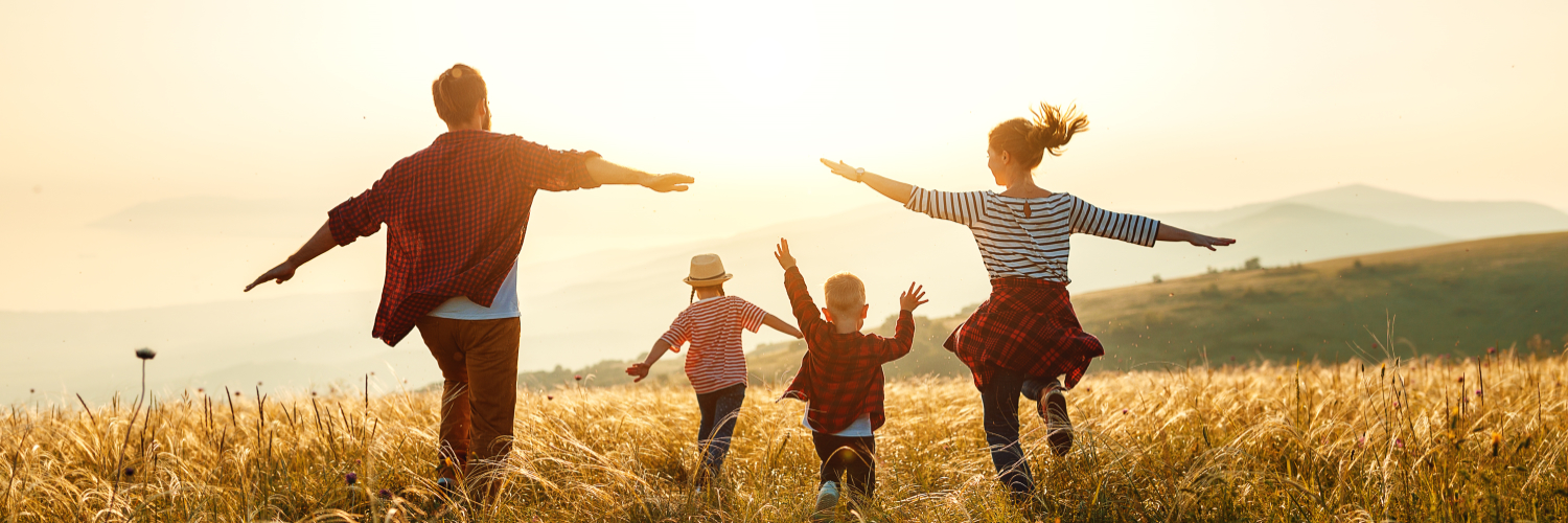 Eine vierköpfige Familie läuft auf einem Feld in Richtung der untergehenden Sonne