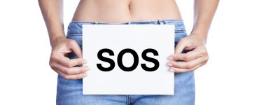 Frau in Jeans hält sich ein SOS-Schild vor die Blase
