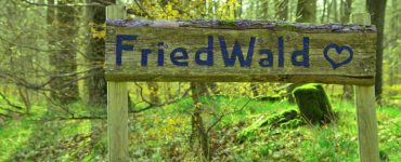 Ein Holzschild in einem blühenden, grünen Wald mit der Aufschrift "FriedWald"