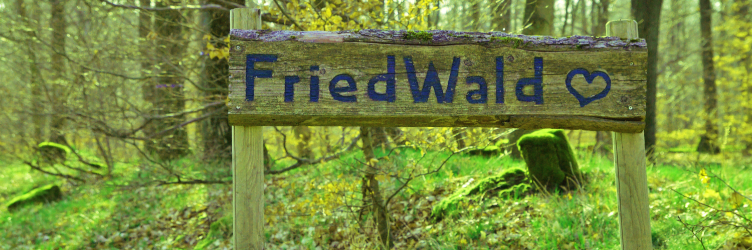 Ein Holzschild in einem blühenden, grünen Wald mit der Aufschrift "FriedWald"