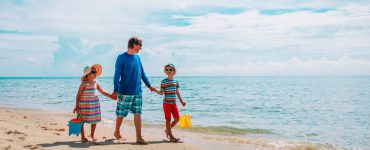 Ein Mensch läuft gemeinsam mit zwei Kindern bei gutem Wetter am Sandstrand