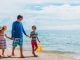 Ein Mensch läuft gemeinsam mit zwei Kindern bei gutem Wetter am Sandstrand