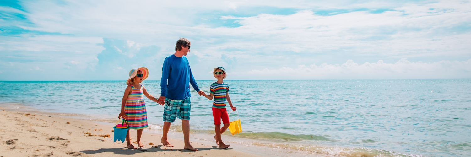 Ein Mensch läuft gemeinsam mit zwei Kindern bei gutem Wetter am Sandstrand