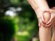 Eine Frau hat schmerzen am Knie und hält es mit beiden Händen