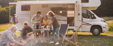 Eine Mehrgenerationen-Familie sitzt und isst draußen vor dem Caravan.