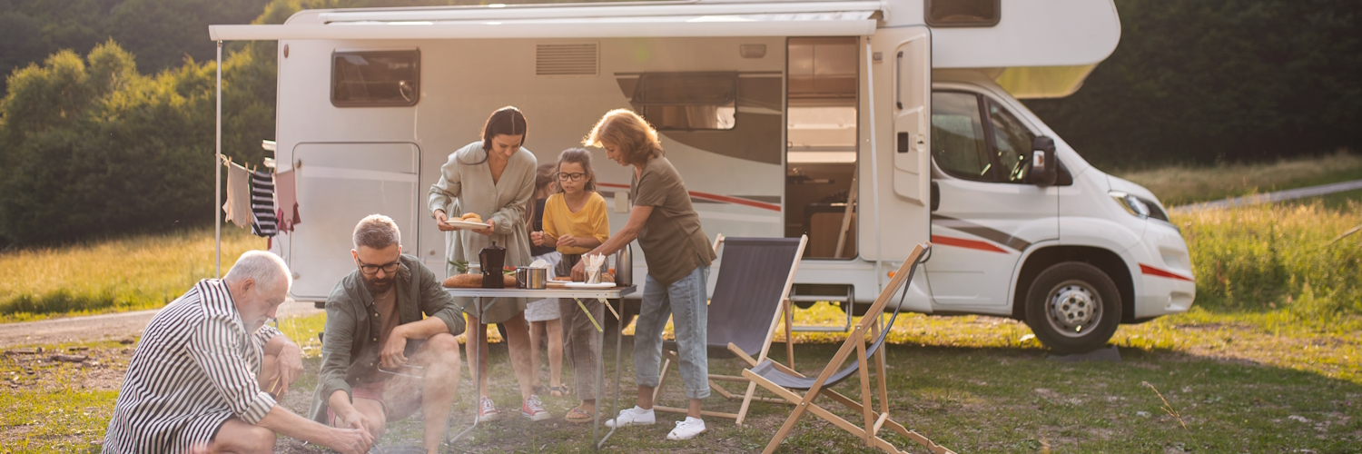 Eine Mehrgenerationen-Familie sitzt und isst draußen vor dem Caravan.