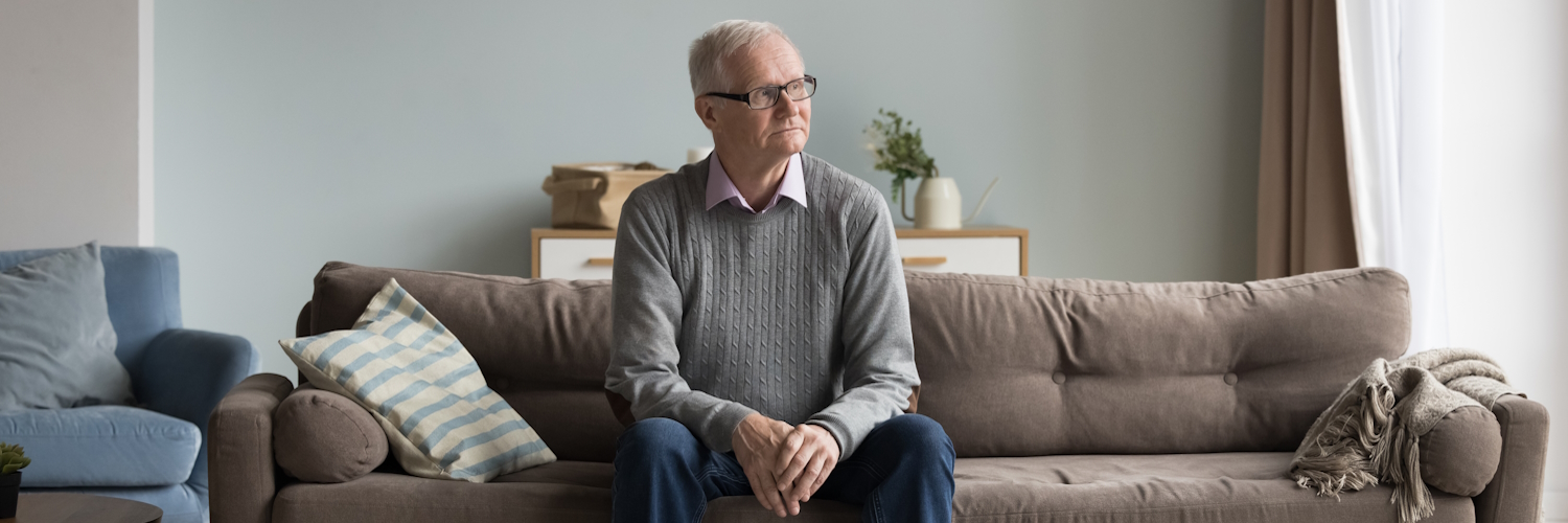 Ein älterer Mensch sitzt nachdenklich auf einem Sofa.