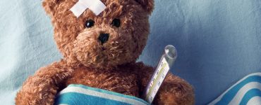 Teddybär mit Pflaster auf dem Kopf und Thermometer im Krankenbett
