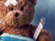 Teddybär mit Pflaster auf dem Kopf und Thermometer im Krankenbett