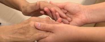 Eine junge Frau hält die Hände einer Seniorin