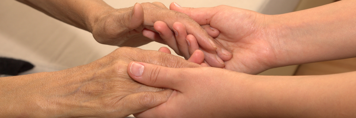 Eine junge Frau hält die Hände einer Seniorin