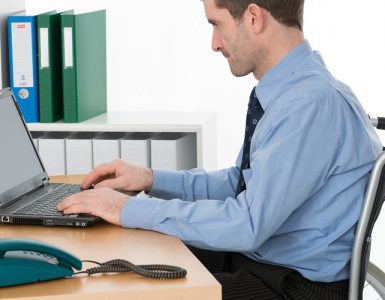 Ein Mensch im Rollstuhl arbeitet an einem Laptop im Büro