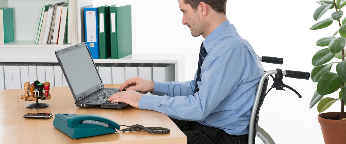 Ein Mensch im Rollstuhl arbeitet an einem Laptop im Büro