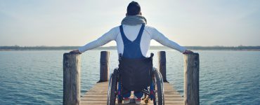Mann in Rollstuhl auf Steg am See