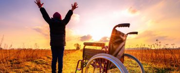 Mensch steht im Sonnenuntergang vor Rollstuhl