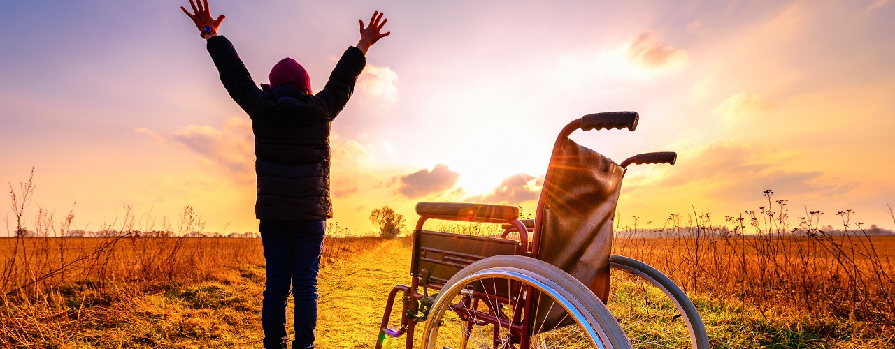 Mensch steht im Sonnenuntergang vor Rollstuhl