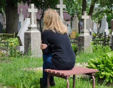 Frau sitzt auf Bank auf Friedhof