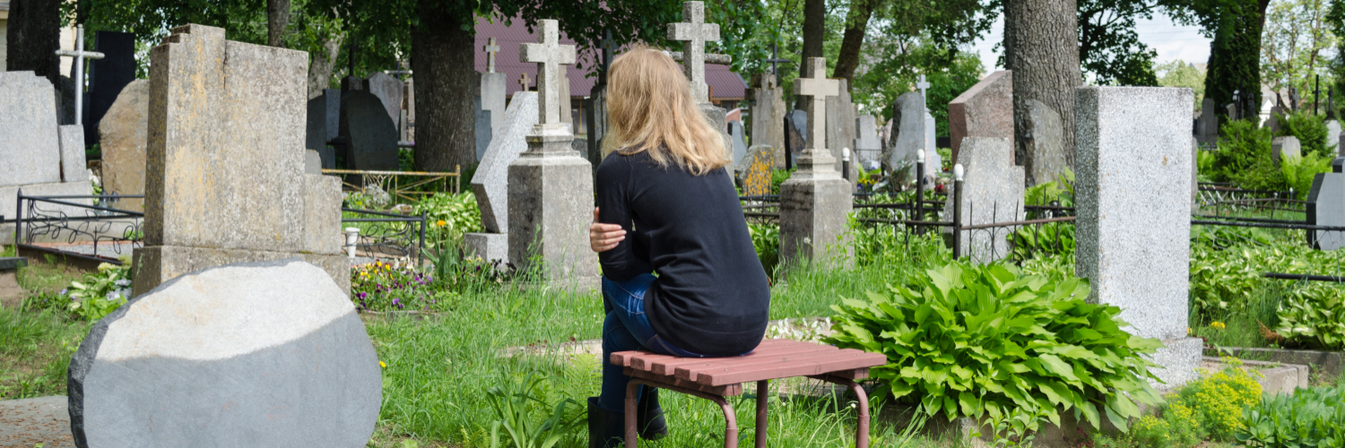 Frau sitzt auf Bank auf Friedhof