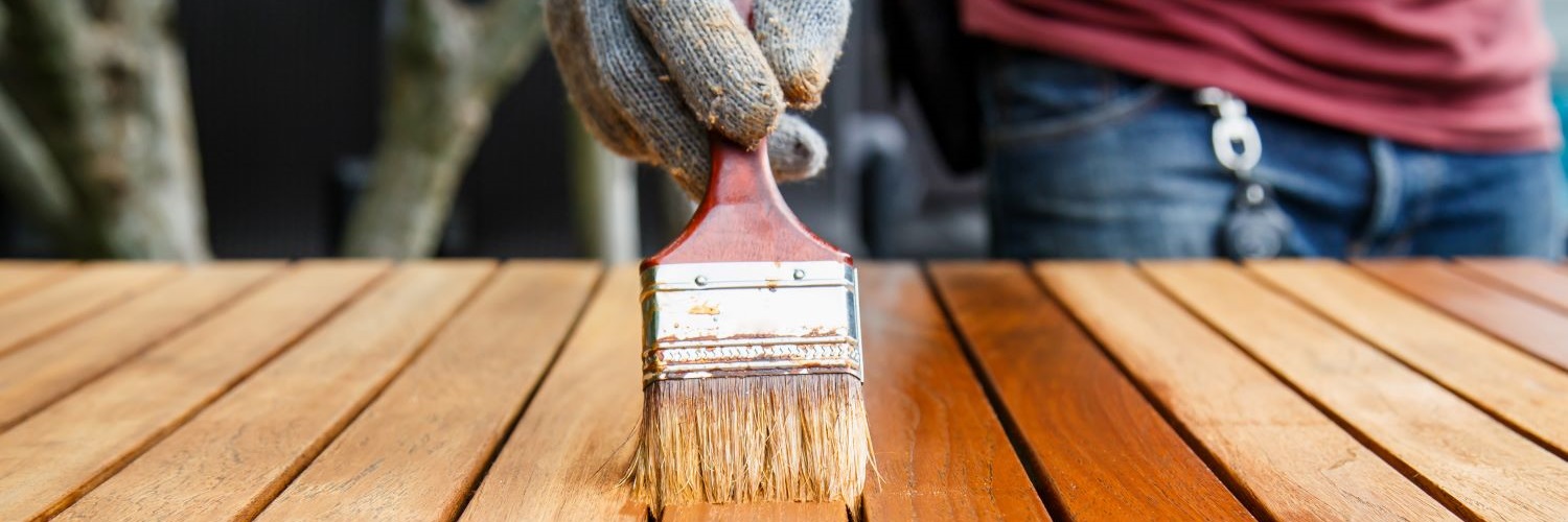 Eine Person leimt mit einem Pinsel einen Holztisch.