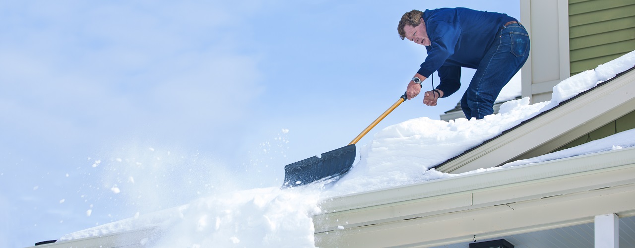 Mann schaufelt Schnee vom Dach