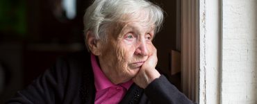 Melancholische alte Frau blickt aus dem Fenster auf der Suche nach einem Weg aus der Einsamkeit