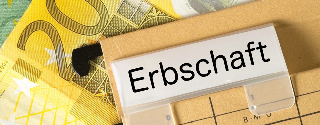 Akte mit der Aufschrift "Erbschaft" vor Geldscheinen im Hintergrund