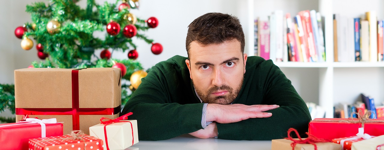 Mann sitzt zwischen Geschenken und hat keine Lust auf Weihnachten