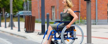 Ein Mensch im Rollstuhl steht an einer Straße und möchte sie überqueren.