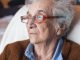 Eine ältere Dame im Krankenbett blickt in die Ferne und wirkt aufgrund der Demenz abwesend