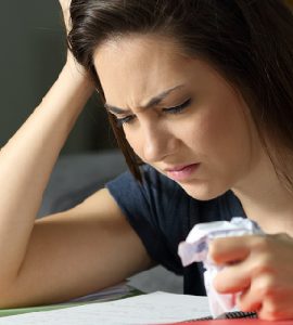 Ein Mensch sitzt angestrengt vor Lehrmaterial. In einer Hand ist ein zerknülltes Papier.