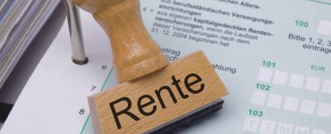 Ein Stempel mit der Aufschrift "Rente" liegt auf einem geöffneten Ordner.